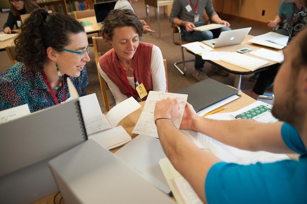 Two women sit across a table from another person who points something out on a document to them. 