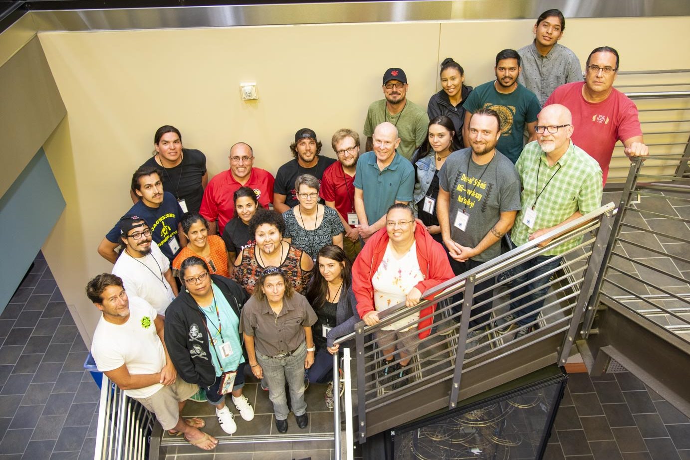 A group of about 25 people stand on a set of stairs, smiling up at the camera. 